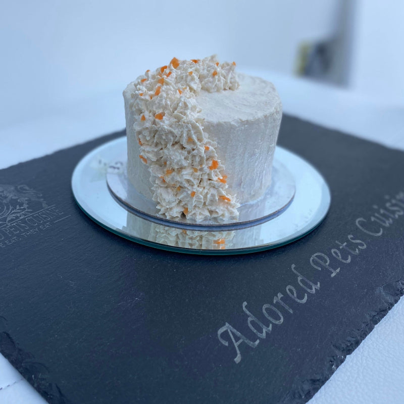 A chicken frosted meat cake for pets, garnished with chicken parfait swirls and fresh carrot, served on a slate board
