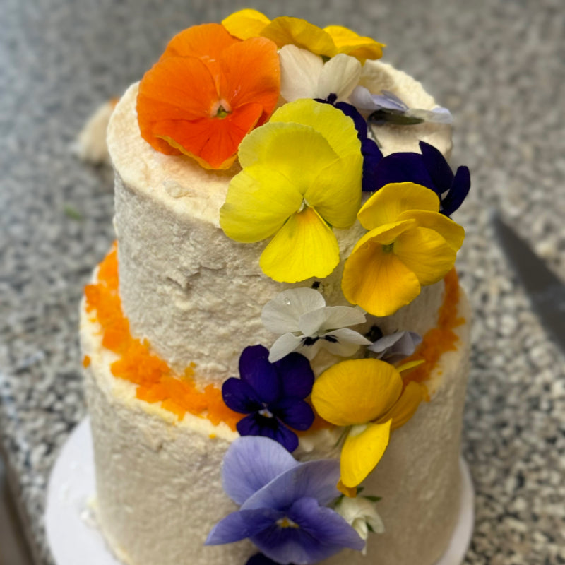 A two-tiered meat cake for pets, coated in chicken frosting and garnished with edible flowers and grated carrot