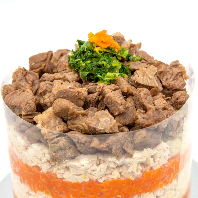 A cake made for pets, with layers of butter baked chicken and carrot, garnished with pieces of steak